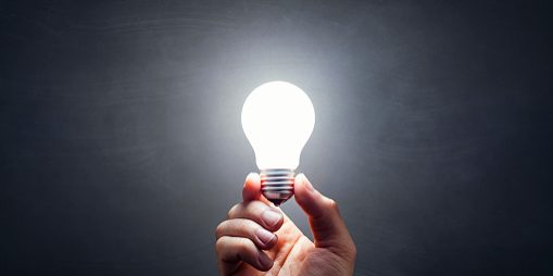 Still life photography of a hand holding a lit light bulb. Smudged blackboard background.